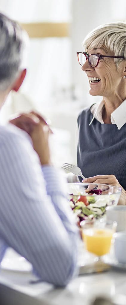 Group of happy business people communicating while having lunch break in cafeteria. Focus is on mature woman.