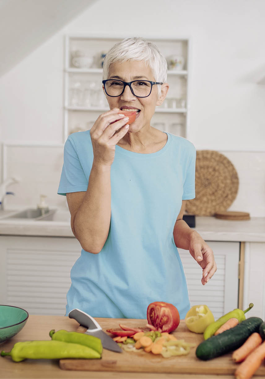Senior woman preparing and tasting vegetables at her kitchen.